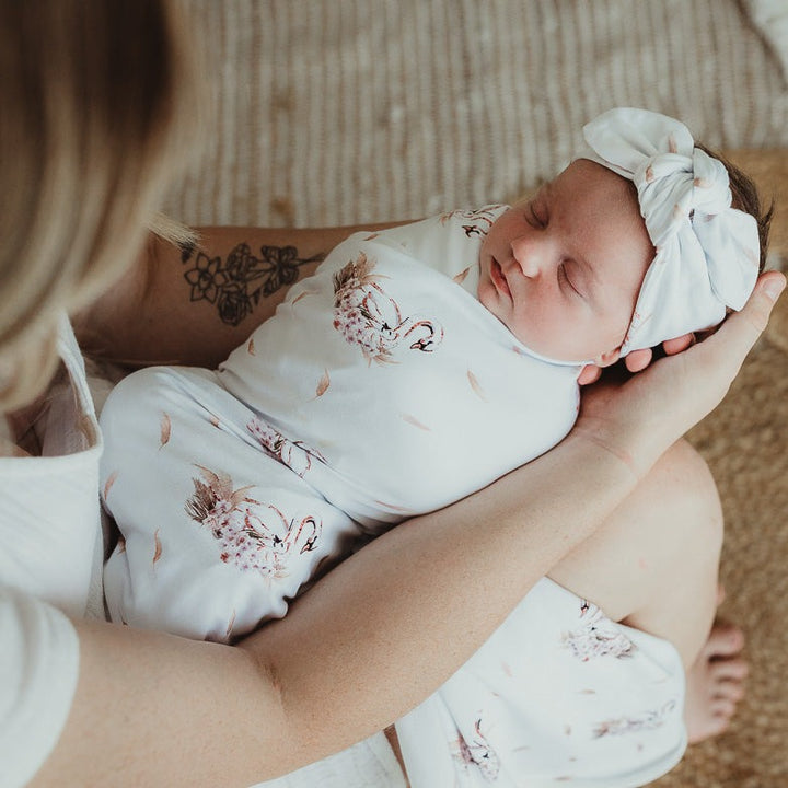 Close up of a sleeping baby wearing a jersey top knot and wrapped in a swaddle being held by mum endearingly