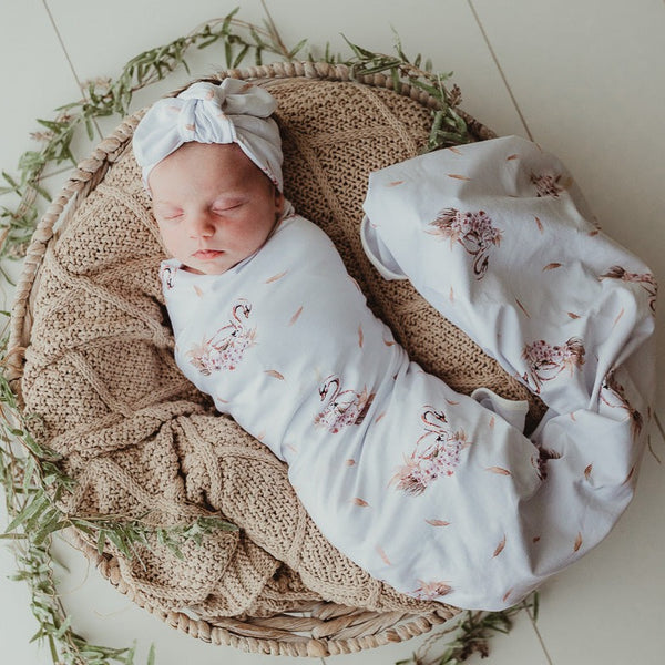 Sweet little baby snuggled in to a taupe knitted blanket and wrapped in a swan printed jersey stretch wrap 