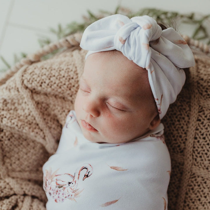 Baby wearing a swan jersey top knot and swaddled in a snuggly jacks stretch wrap