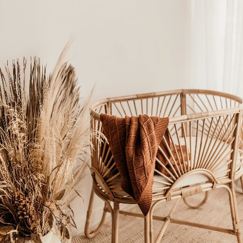 White room with a rattan bassinet with a snuggly jacks organic knitted blanket in cinnamon draped over the side