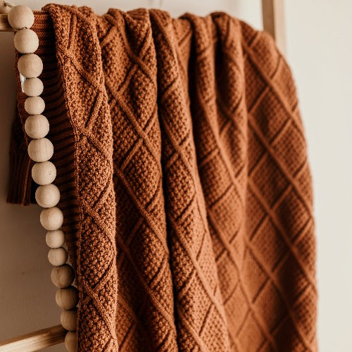 rattan ladder with a snuggly jacks organic knitted blanket in cinnamon draped over the side