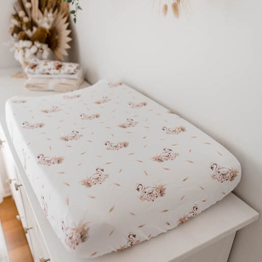 White change mat cover with soft pink swans placed in a seamless pattern set out on a whit pine change table.