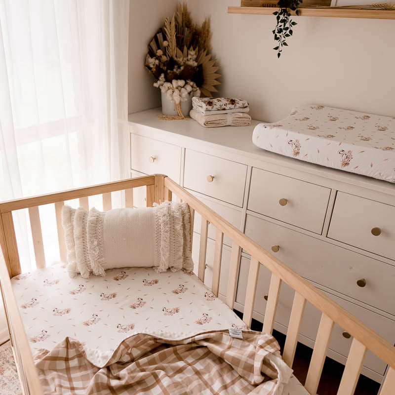 Stylish nursery set with swan prints on the sheets and change mat, illustrating a way you can bring brown hues to your babies space.
