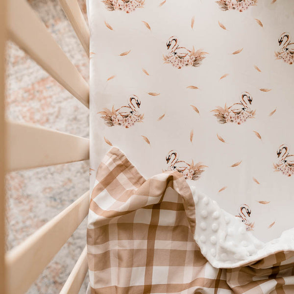 Elegant swan print on a 100% cotton sheet depicted in a pine cot, there is a soft brown dimple dot minky draped over the sheet.