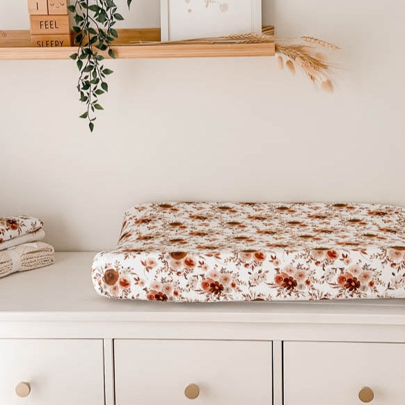 White change table with floral burp cloths on one side and a change mat covered by a 100% cotton cover 