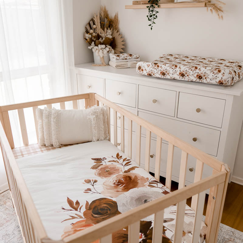 modern nursery with a cot set using a cot quilt with a large floral print and in the back ground a change mat with a warm floral printed change mat cover.